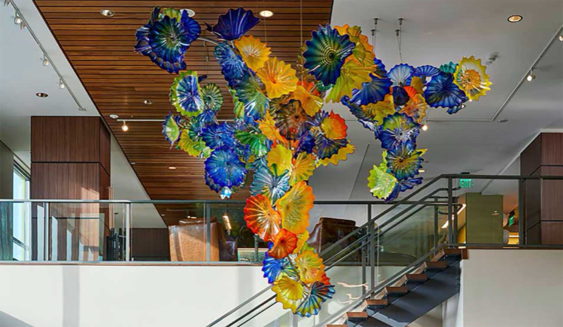 Colorful blown-glass chandelier suspended above the lobby staircase at Murano Senior Living
