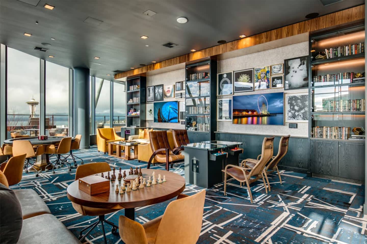 Resident lounge with a chess table, arcade cabinet, and floor-to-ceiling views of the Space Needle