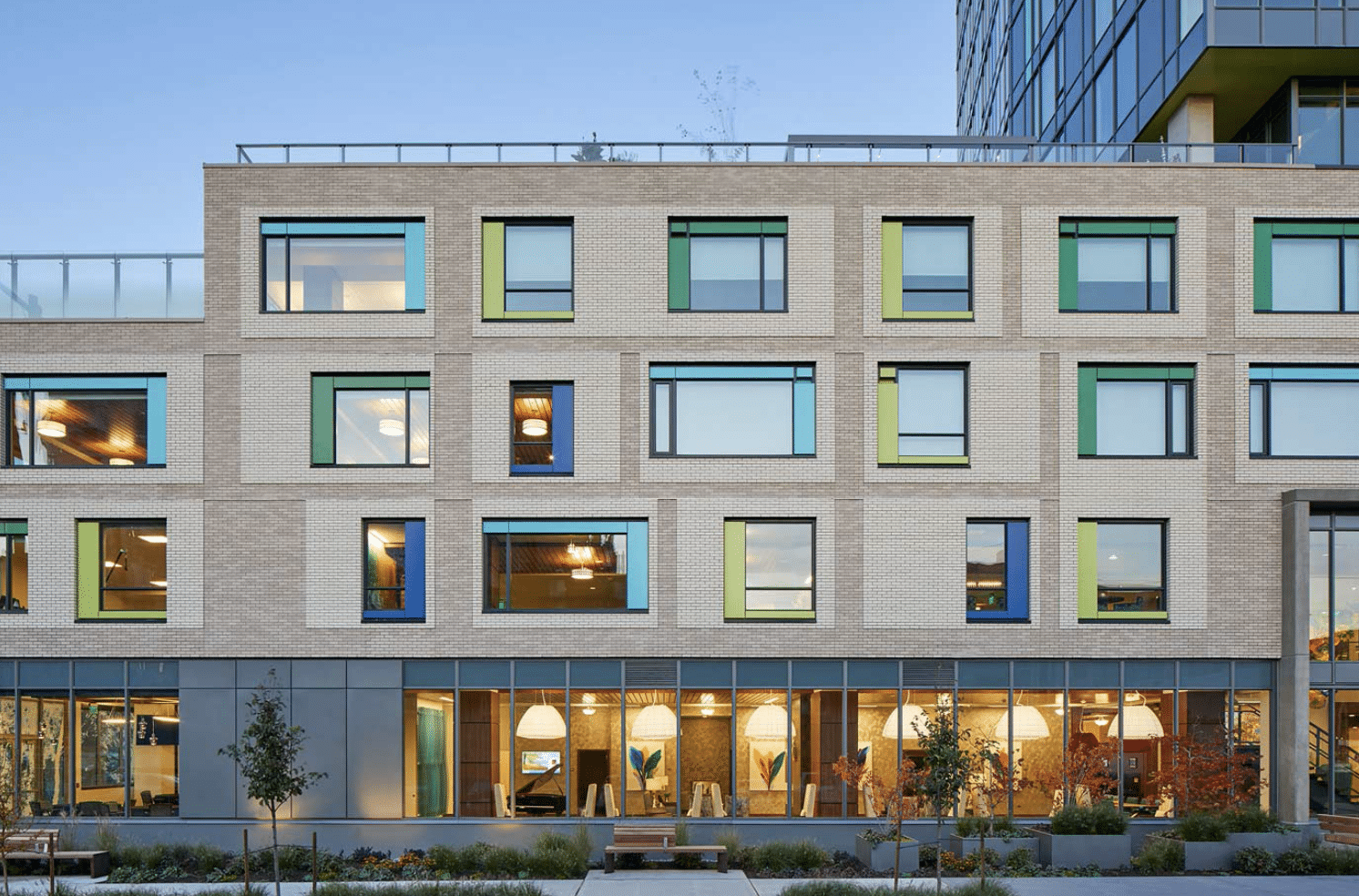 Light brick senior living facade with color-framed windows above a glass-walled ground floor