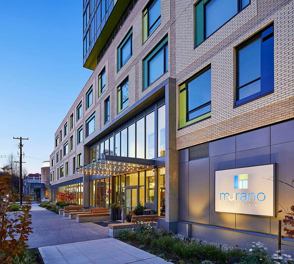 Entrance to Murano Senior Living with a lit canopy and colorful window frames
