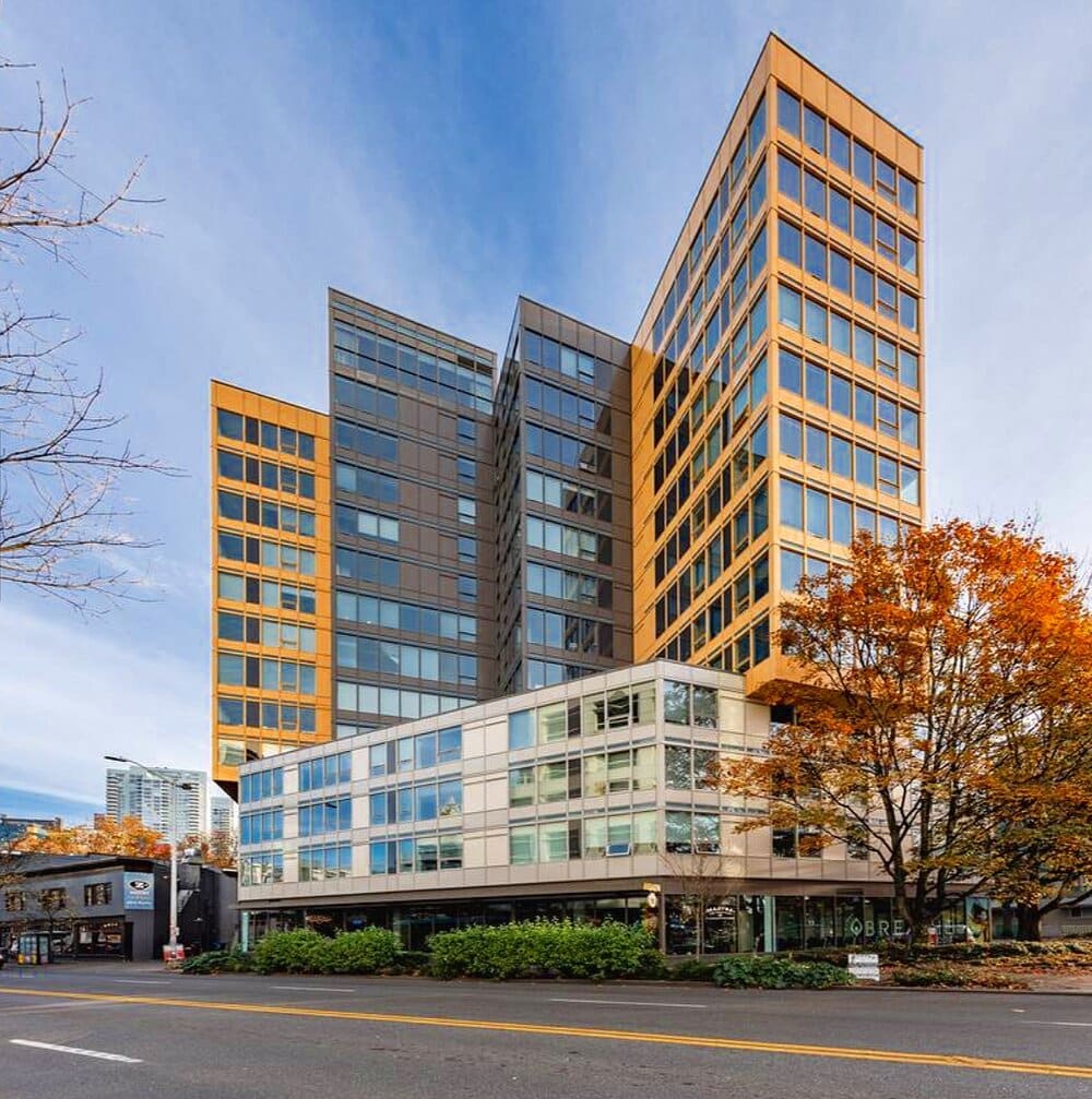 Gold and charcoal mid-rise towers above street-level retail in autumn