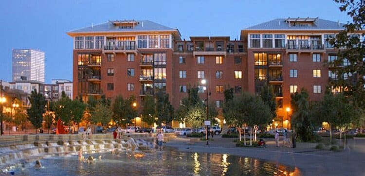 Brick apartment buildings beside a waterfront park fountain at dusk